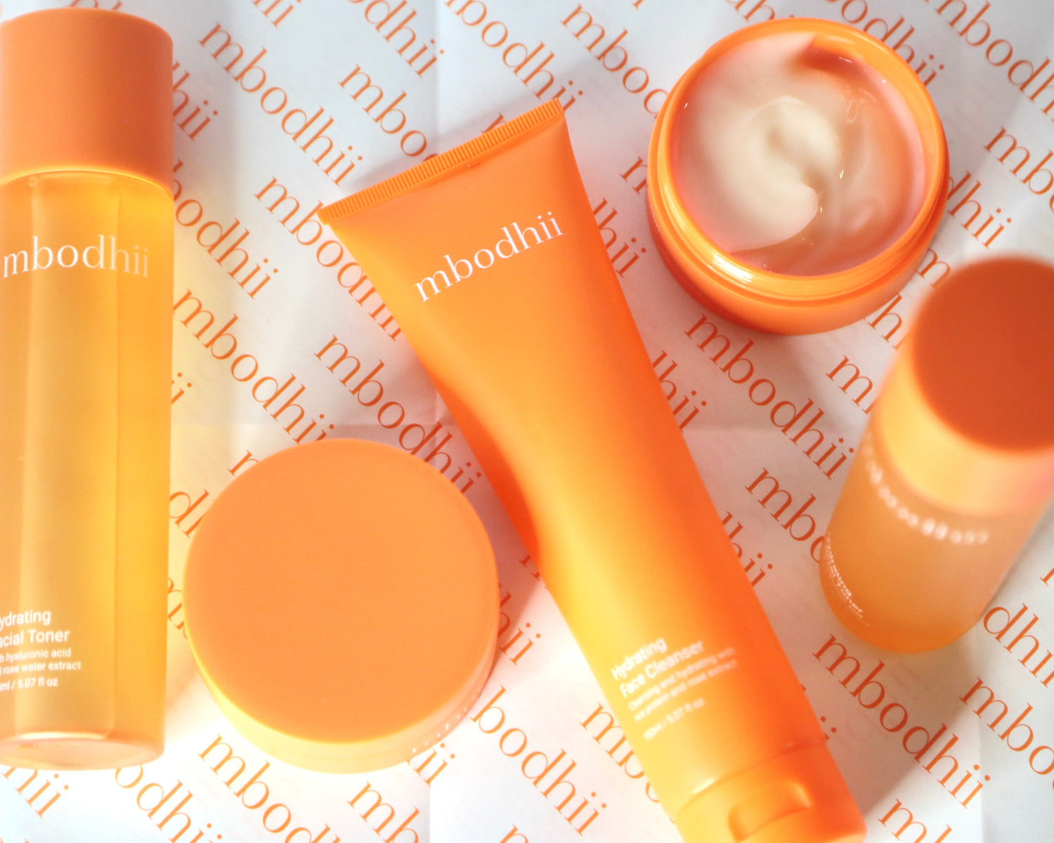 A collection of mbodhii products laid flat on a table with the face cream open so you can see it's luxurious texture.