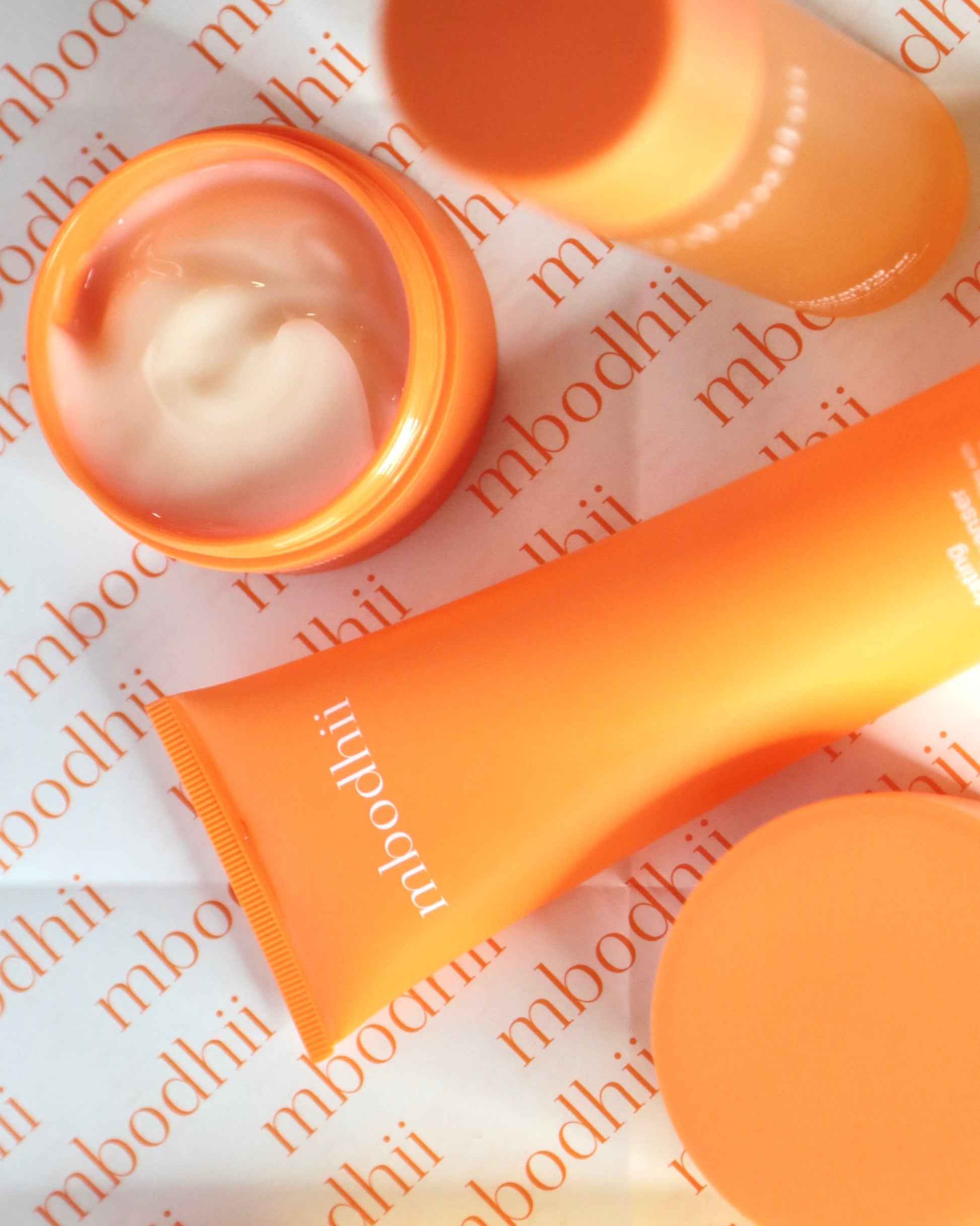 The mbodhii Hydra Glow Essentials Pack laid out on a table top with branded tissue paper in the background. The Face Cream is open so you can see the creamy texture.