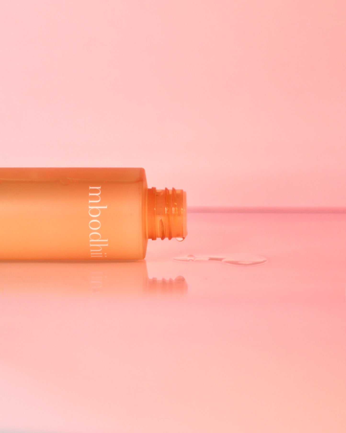 The mbodhii Hydrating Facial Toner bottle on it's side with toner dripping out onto a table