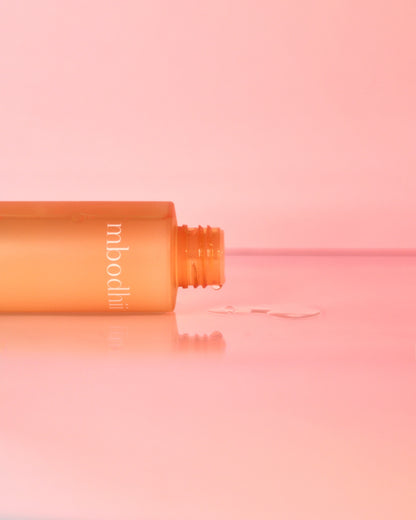The mbodhii Hydrating Facial Toner bottle on it's side with toner dripping out onto a table