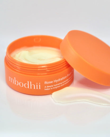 Open jar of mbodhii Rose Hydrating Face Cream with orange lid on a light gray background with cream visable